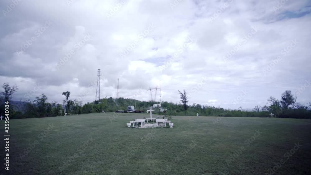 SLOW MOTION: wide push straight towards and through a set of pews in front of a white cross standing on a mountain top in Juana Diaz, Puerto Rico on an overcast day. SLOW MOTION: wide push straight towards and through a set of pews in front of a white cross standing on a mountain top in Juana Diaz, Puerto Rico on an overcast day.