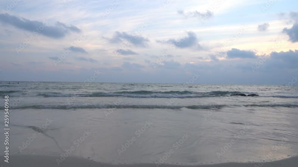 Medium angle shot of waves gently rolling onto an empty sandy beach during a cloudy sunset Medium angle shot of waves gently rolling onto an empty sandy beach during a cloudy sunset