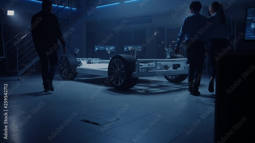 Automobile Design Engineers Talking while Working on Electric Car Chassis Prototype. In Automotive Innovation Facility Concept Vehicle Frame Includes Tires, Suspension, Engine and Battery Automobile Design Engineers Talking while Working on Electric Car Chassis Prototype. In Automotive Innovation Facility Concept Vehicle Frame Includes Tires, Suspension, Engine and Battery
