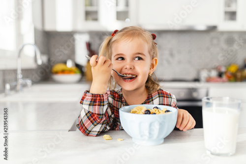 Beautiful little girl having breakfast with cereal, milk and blueberry in kitchen