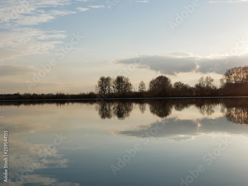 Polonne / Ukraine - 18 February 2019: Scenic river reflections of trees on the water. A river with trees on the shores. Reflection of blue sky with clouds in calm water
