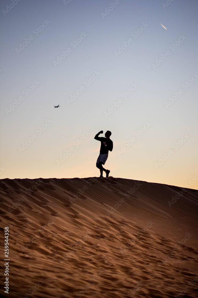Dark silhouette of a man walking at the desert dunes. Dawn time