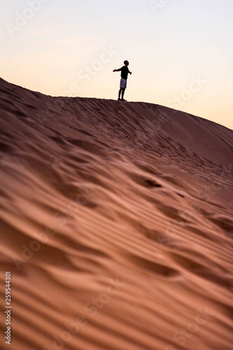 Dark silhouette of a man walking at the desert dunes. Dawn time. Holding hands imagine flying, dreaming and breathing deep