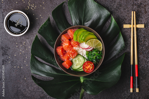 Hawaiian salmon poke salad with rice, avocado and seaweed served in bowl on tropical leaves photo