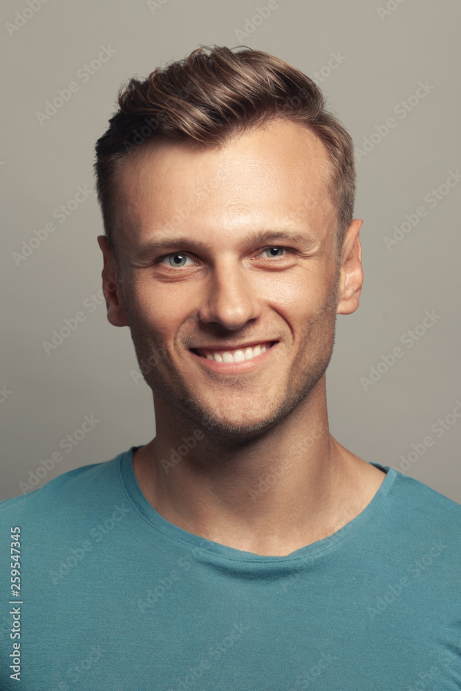 Obraz premium Male beauty, boy next door concept. Portrait of smiling 30-year-old man standing over gray background. Close up. Classic style. Wavy glossy blond hair. Studio shot