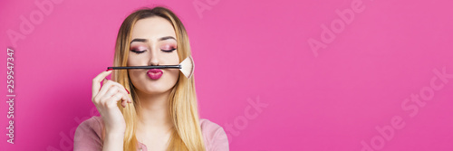funny portrait of a beautiful young girl with makeup brush in a studio, woman face, cosmetics and natural beauty concept