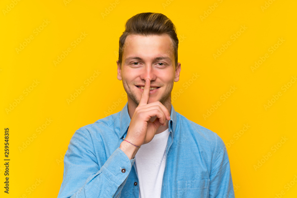 Blonde handsome man over isolated wall doing silence gesture