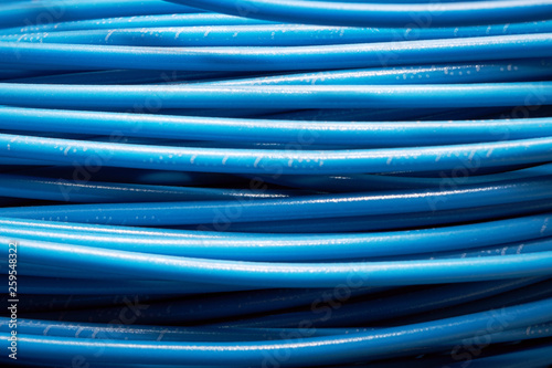 A pile or stack of blue electrical wires. Flexible stranded wires or cables lie horizontally. Background, backdrop, texture. New wires for electrical appliances and equipment.
