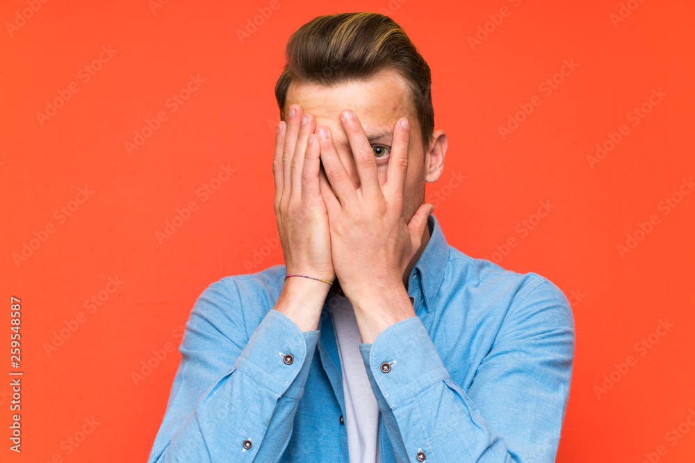 Blonde handsome man over isolated wall covering eyes and looking through fingers Blonde handsome man over isolated wall covering eyes and looking through fingers