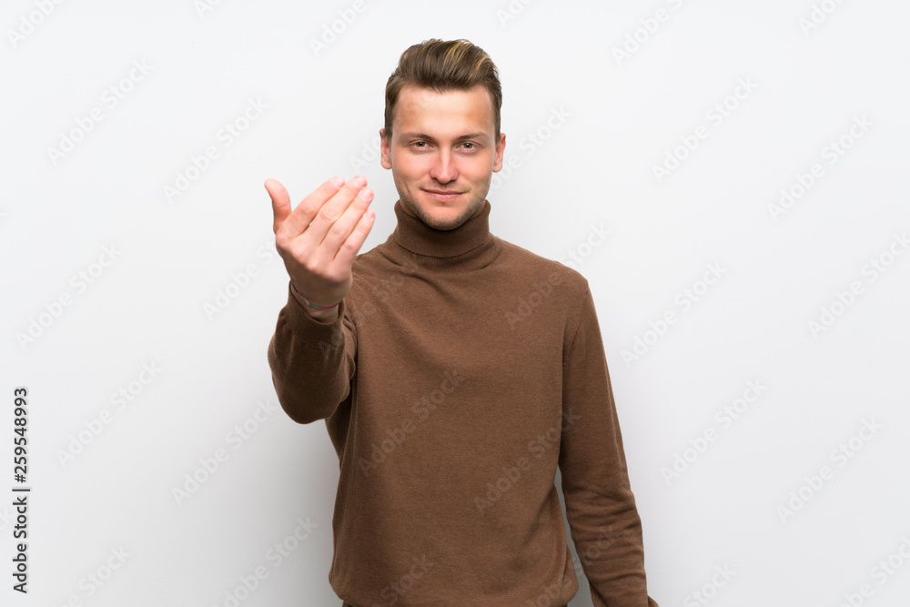 Blonde man over isolated white wall inviting to come with hand. Happy that you came Blonde man over isolated white wall inviting to come with hand. Happy that you came