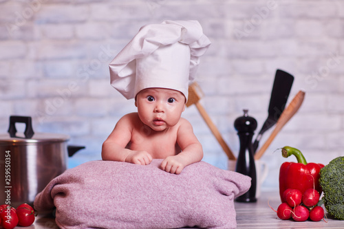 Child, baby girl lies on the kitchen table in a chef's cap - next to him are vegetables, bell pepper, radish, broccoli, proper nutrition, vegetarianism