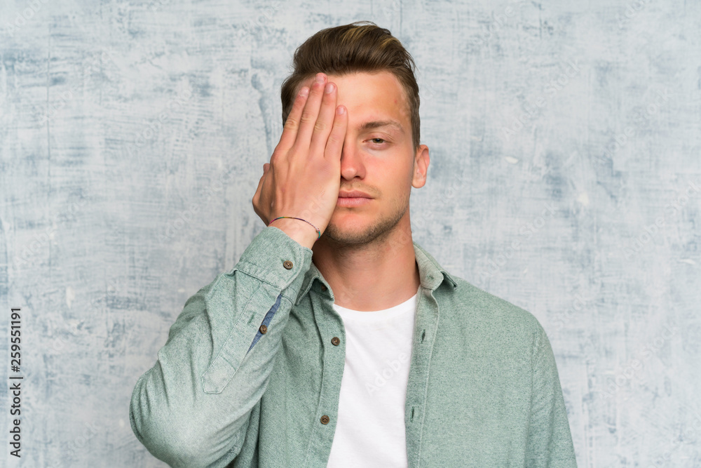 Blonde handsome man with green shirt covering a eye by hand Blonde handsome man with green shirt covering a eye by hand