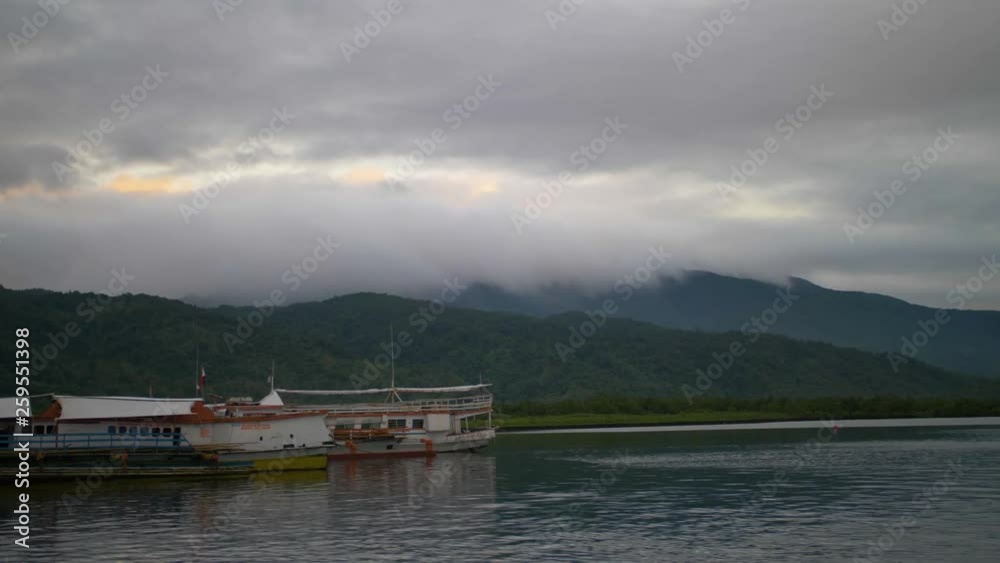 View from a ferry departing a harbor in the Philippines on a cloudy, overcast morning. Mountains hidden in clouds and fog in the distance. View from a ferry departing a harbor in the Philippines on a cloudy, overcast morning. Mountains hidden in clouds and fog in the distance.