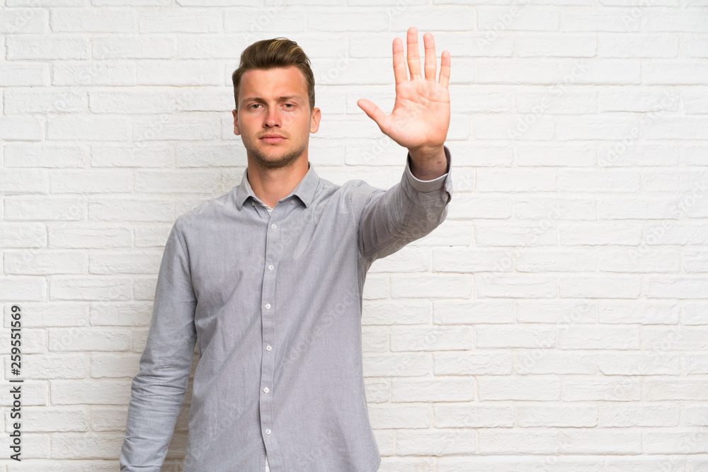 Blonde man over white brick wall making stop gesture Blonde man over white brick wall making stop gesture