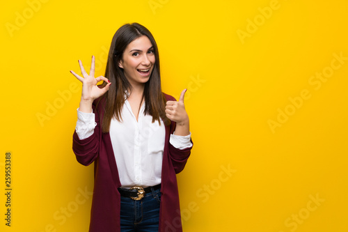 Young woman over yellow wall showing ok sign with and giving a thumb up gesture photo