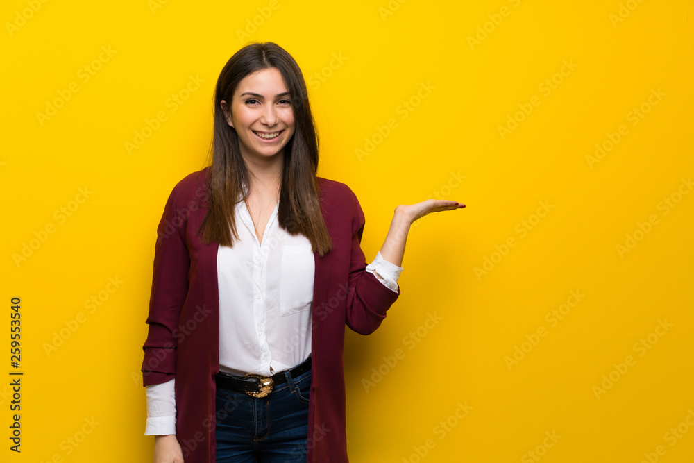 Young woman over yellow wall holding copyspace imaginary on the palm to insert an ad Young woman over yellow wall holding copyspace imaginary on the palm to insert an ad
