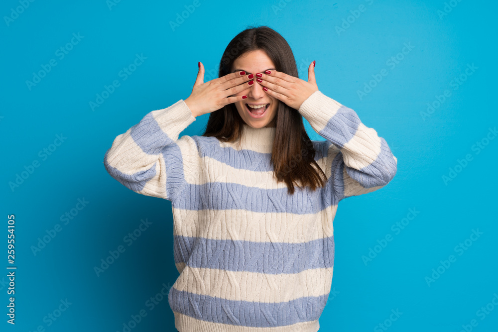 Fototapeta premium Young woman over blue wall covering eyes by hands. Surprised to see what is ahead