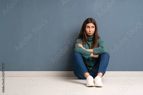 Young woman sitting on the floor making doubts gesture while lifting the shoulders