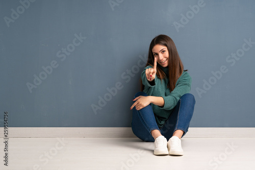Young woman sitting on the floor showing and lifting a finger