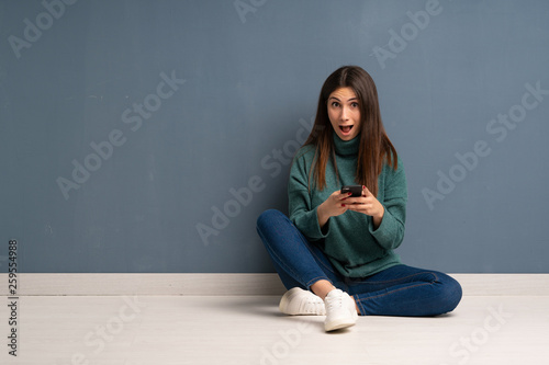 Young woman sitting on the floor surprised and sending a message