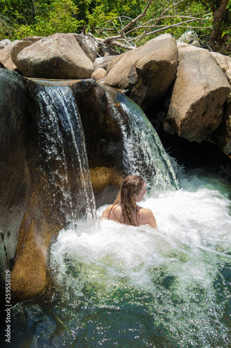 Girl swimming and relaxing in a waterfall in wild nature among big stones.