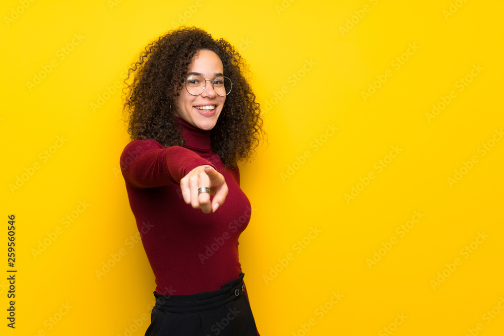 Dominican woman with turtleneck sweater points finger at you with a confident expression Dominican woman with turtleneck sweater points finger at you with a confident expression