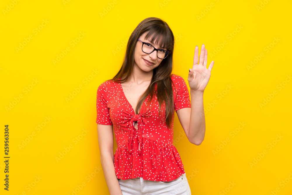 Young woman over yellow wall saluting with hand with happy expression Young woman over yellow wall saluting with hand with happy expression