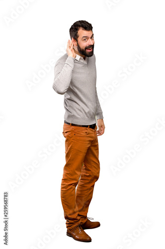Handsome man listening to something by putting hand on the ear over isolated white background