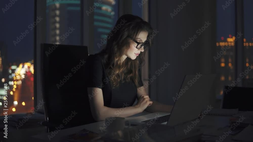young business woman working late in the office. portrait of a girl with glasses on the background of the night city