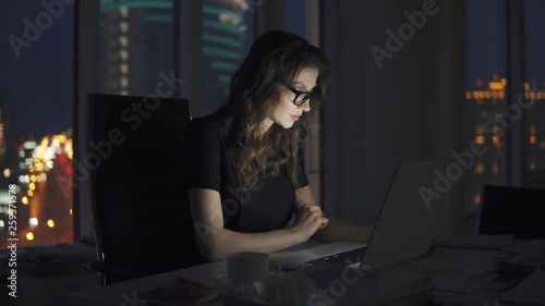 young business woman working late in the office. portrait of a girl with glasses on the background of the night city