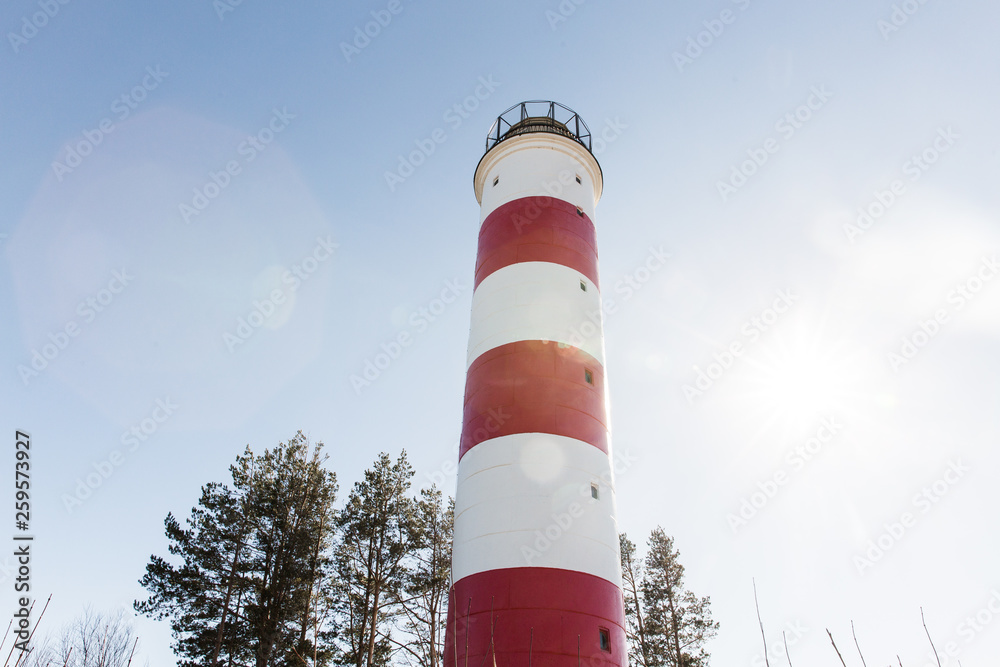white and red striped beacon on the coastline on blue sky background. lighthouse white and red striped beacon on the coastline on blue sky background. lighthouse