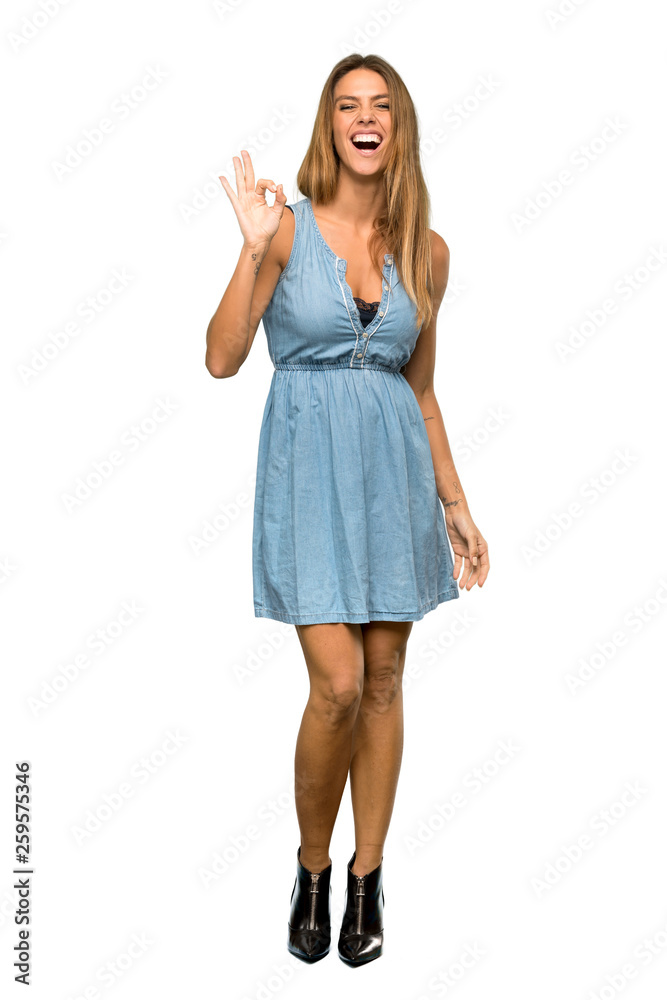 A full-length shot of a Blonde woman with jean dress showing ok sign with fingers over isolated white background A full-length shot of a Blonde woman with jean dress showing ok sign with fingers over isolated white background