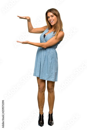 A full-length shot of a Blonde woman with jean dress holding copyspace to insert an ad over isolated white background