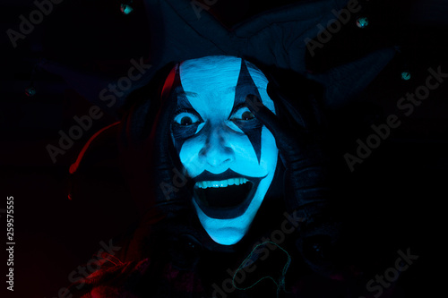 Horrible screaming jester's face in dark room, close-up.