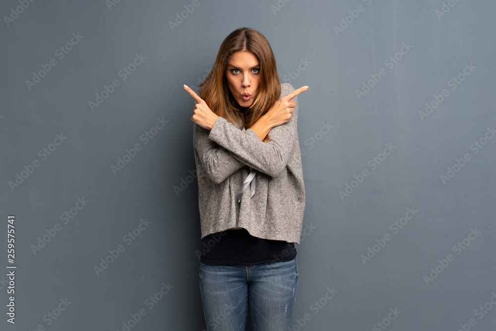 Blonde woman over grey background pointing to the laterals having doubts Blonde woman over grey background pointing to the laterals having doubts