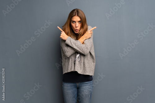 Blonde woman over grey background pointing to the laterals having doubts