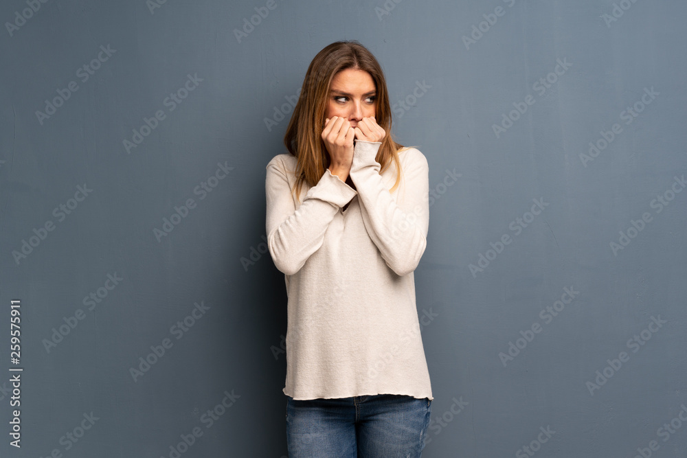 Blonde woman over grey background nervous and scared putting hands to mouth Blonde woman over grey background nervous and scared putting hands to mouth