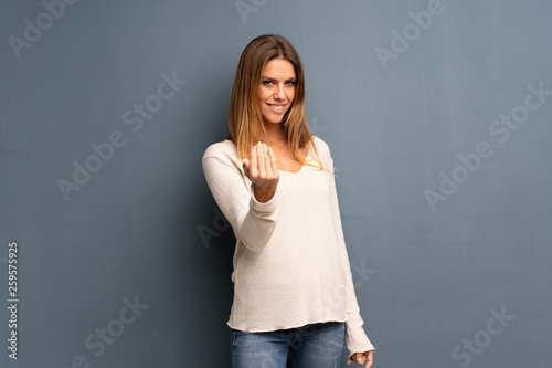 Blonde woman over grey background inviting to come with hand. Happy that you came