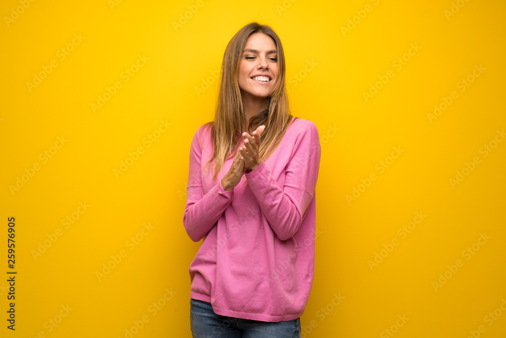Woman with pink sweater over yellow wall applauding after presentation in a conference Woman with pink sweater over yellow wall applauding after presentation in a conference