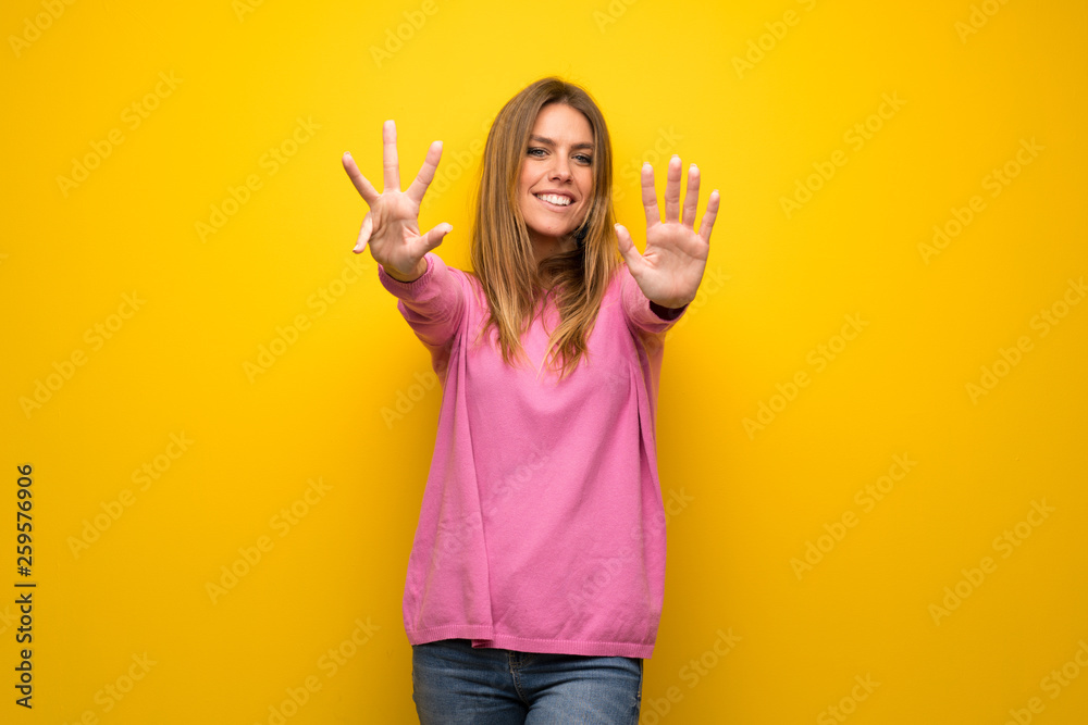Woman with pink sweater over yellow wall counting nine with fingers