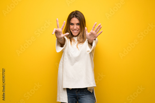 Blonde woman over yellow wall counting eight with fingers