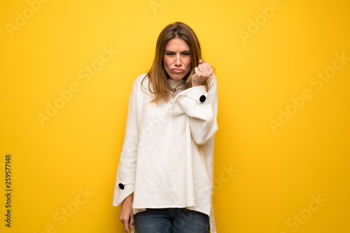 Blonde woman over yellow wall with angry gesture