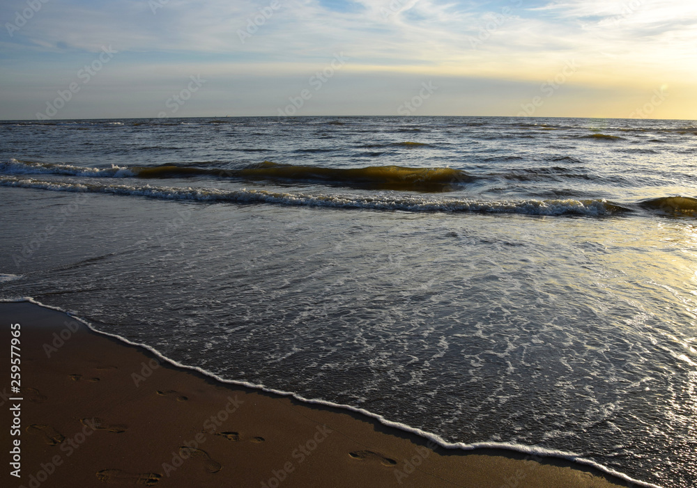 Sunset over the Ocean - View of the red sun sinking into the horizon and waves washing over the sand of the beach