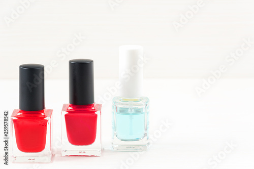 Close-up image of Two Red nail polish bottles and one colorless nail polish bottle on white wooden background.