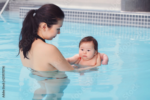Mixed race asian mother traning her newborn baby to float in swimming pool. Baby diving in water. Healthy active lifestyle. Family activity and early development concept © anoushkatoronto