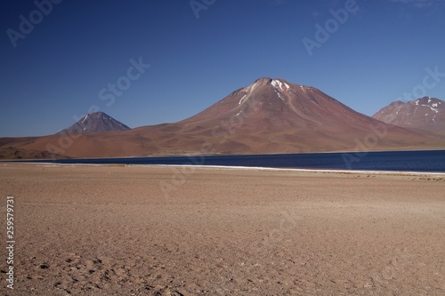 View on deep blue lake at Altiplanic Laguna (Lagoon) Miscanti in Atacama desert with partly snow capped cone of volcano Meniques in the background - Chile photo