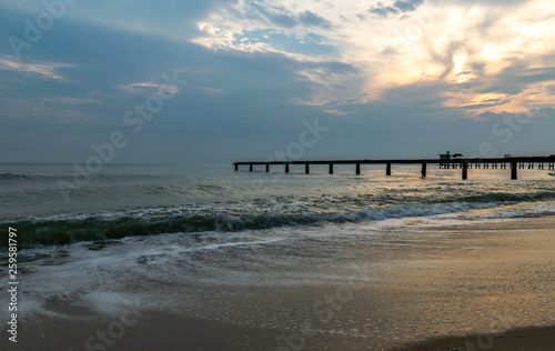 Old stone bridge into the sea and Sea waves is in the foreground.