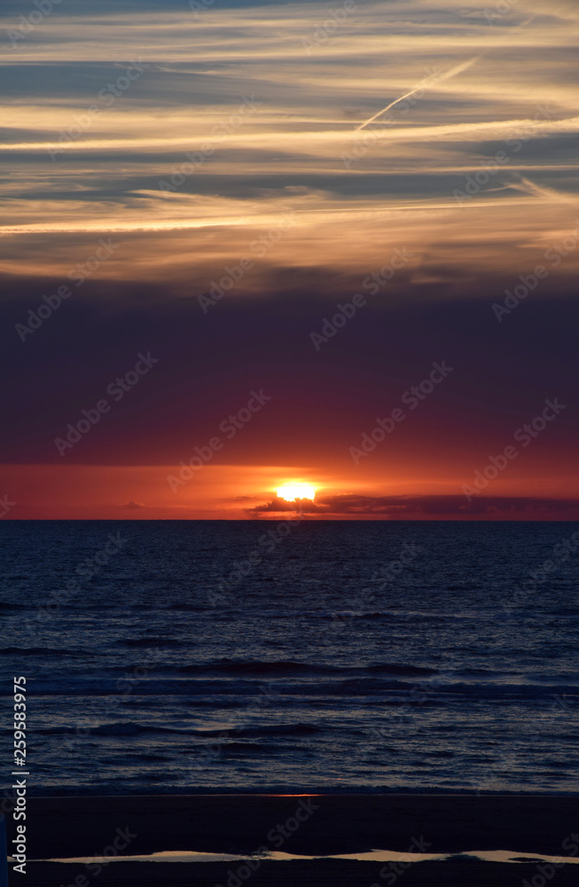 Sunset over the Ocean - View of the red sun sinking into the horizon and waves washing over the sand of the beach