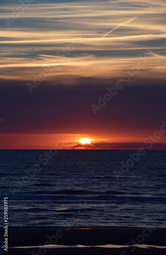 Sunset over the Ocean - View of the red sun sinking into the horizon and waves washing over the sand of the beach