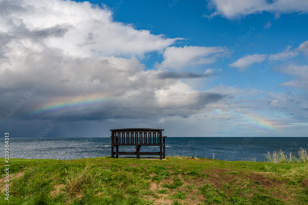 A bench with a Rainbow over the North Sea coast, seen in Benthall, Northumberland, England, UK A bench with a Rainbow over the North Sea coast, seen in Benthall, Northumberland, England, UK